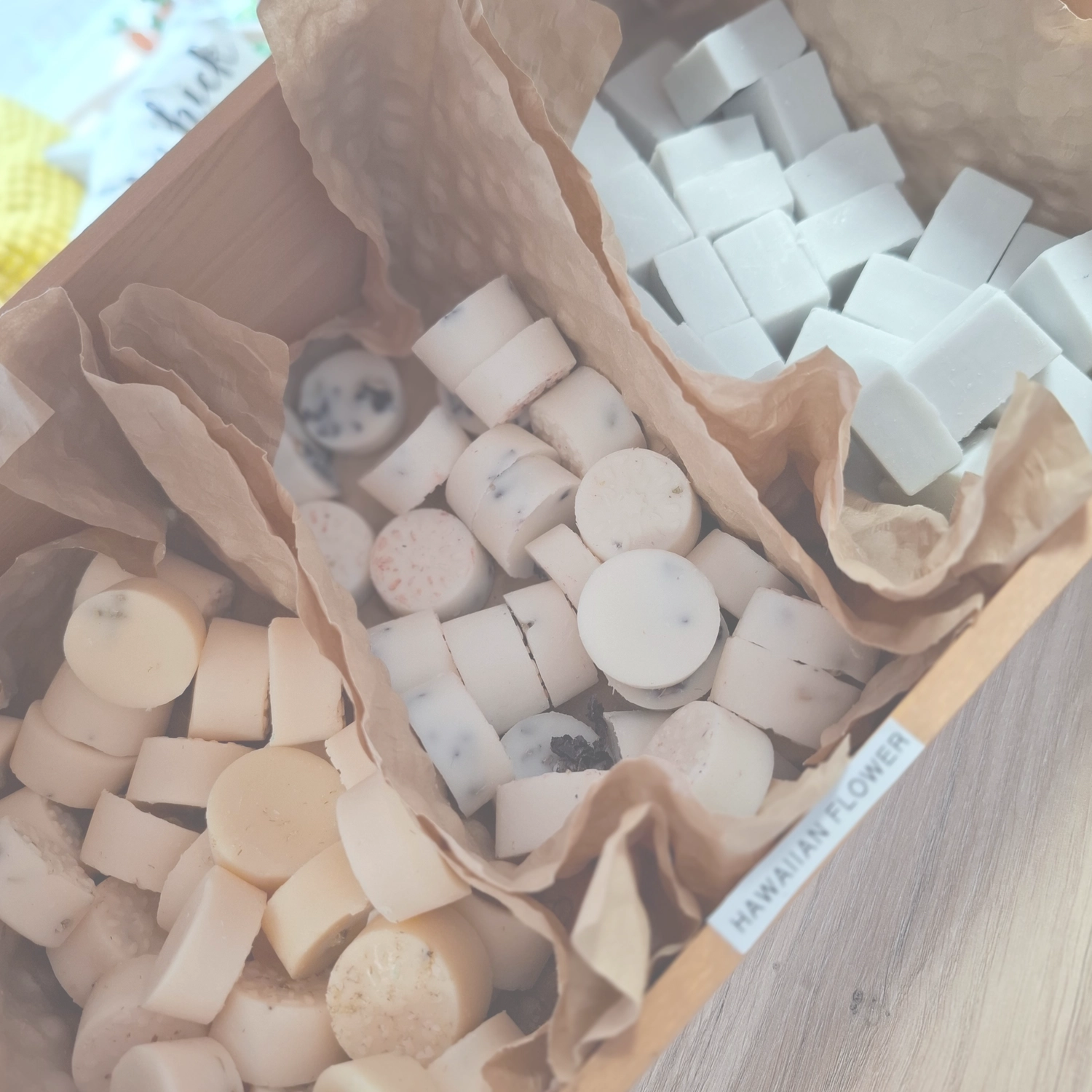 Grace&Felicity - concept store - Eine Nahaufnahme von weißen, quadratischen Wachsmelts oder Seifen, die in braunes Knüllpapier eingebettet sind.