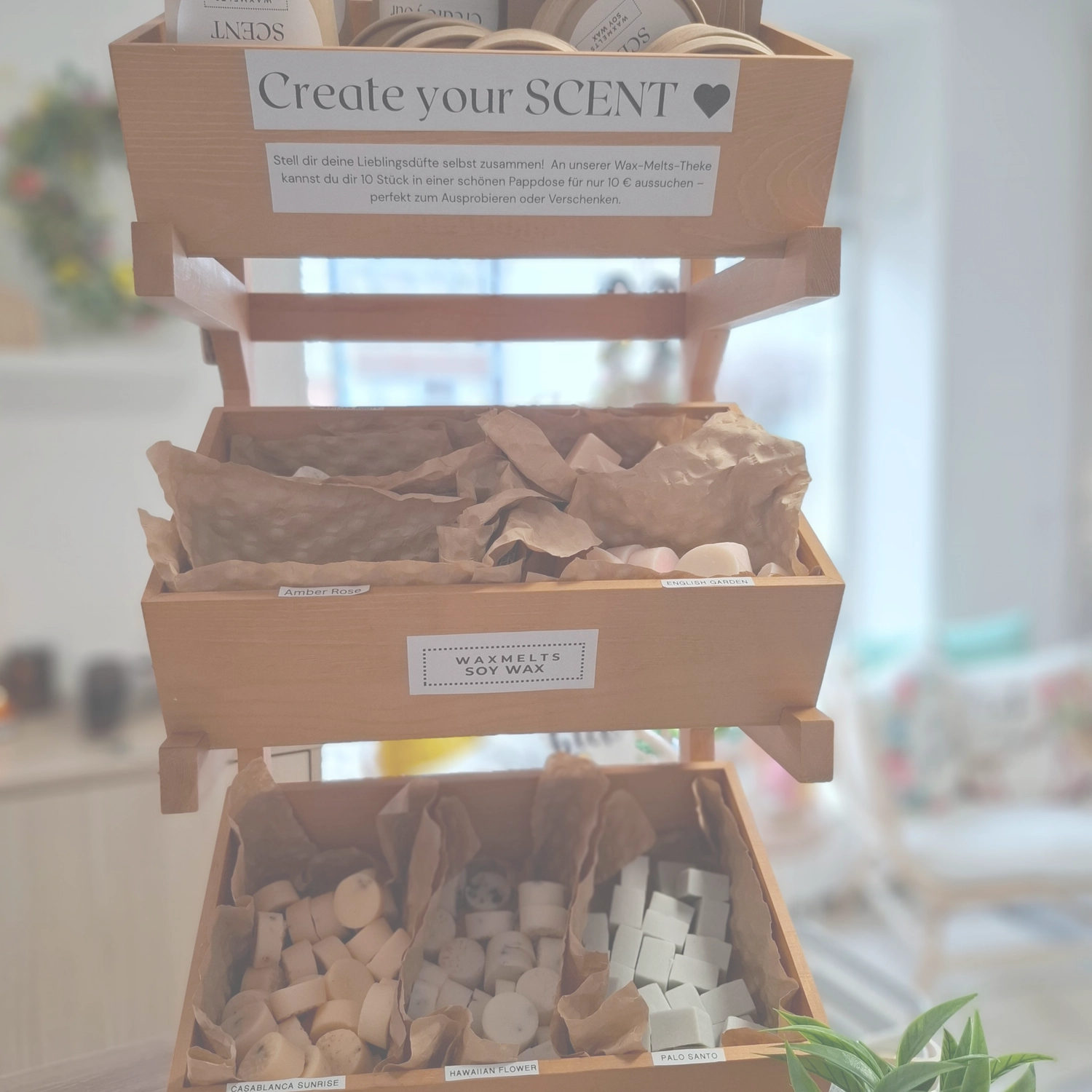 Grace&Felicity - concept store - Ein Pappaufsteller mit der Aufschrift „Kreieren Sie Ihren Duft“ über einem Behälter mit in braunes Papier eingewickelten Duftartikeln.
