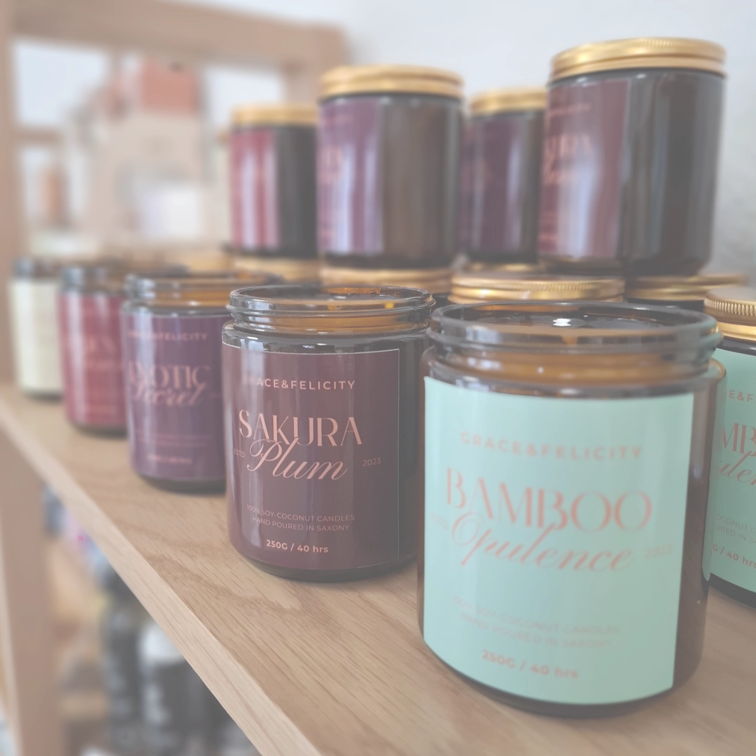 Grace&Felicity - concept store -Leicht unscharfe Aufnahme von mehreren Duftkerzen in dunkelbernsteinfarbenen Glasgefäßen mit goldenen Deckeln.