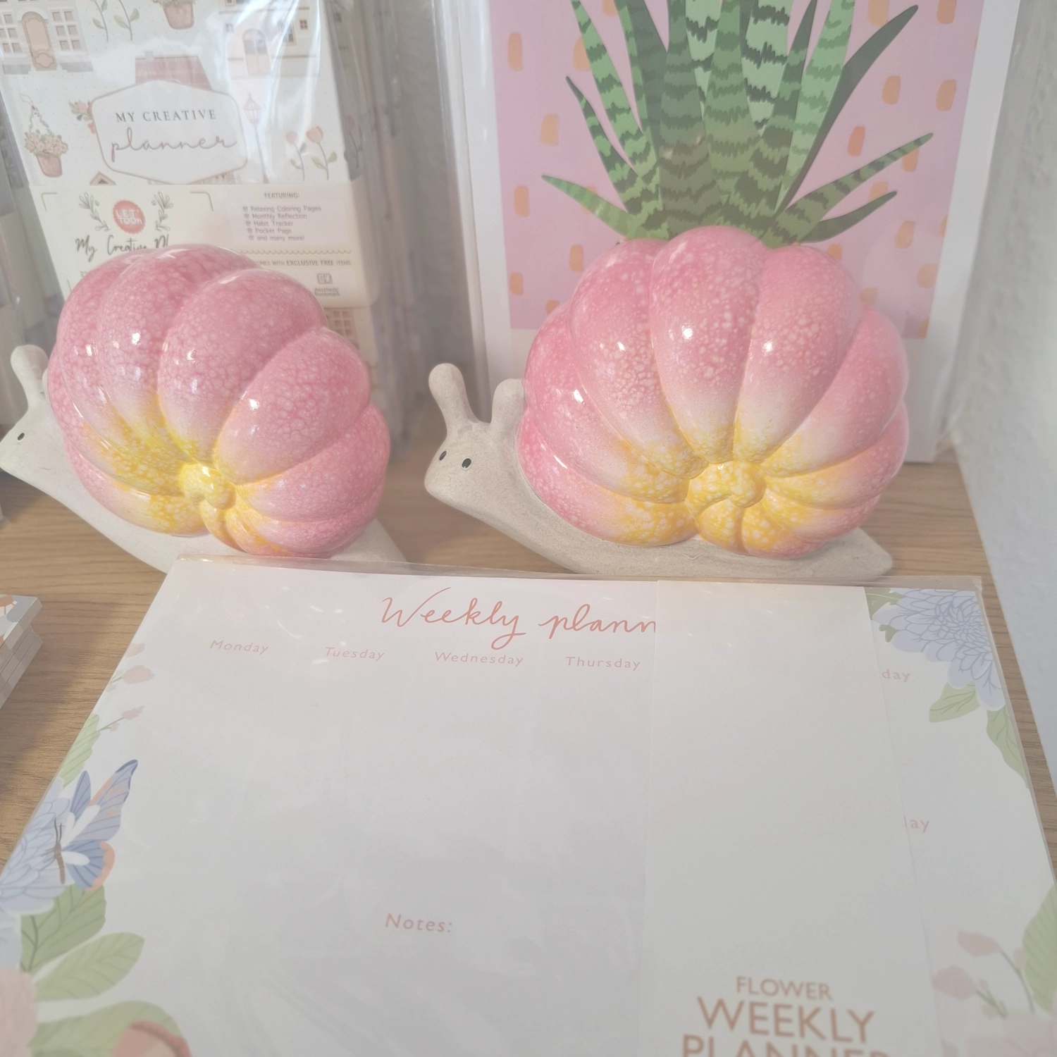 Grace&Felicity - concept store - Eine Sammlung skurriler, rosafarbener, schneckenförmiger Keramikgefäße oder Pflanzgefäße steht auf einem Schreibtisch neben einem Notizblock mit der Aufschrift „Wochenplan“.