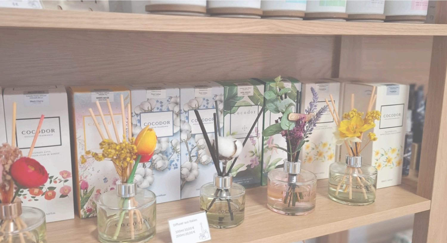 Grace&Felicity - concept store -  Ein Holzregal mit Cocodor-Raumduftstäbchen in Glasflaschen, verziert mit bunten Trockenblumen und -stängeln.