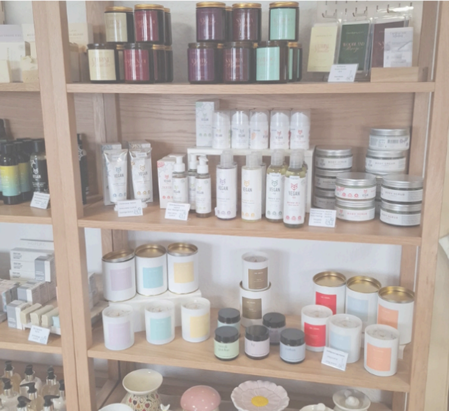 Grace&Felicity - concept store - Ein mehrstöckiges Holzregal, gefüllt mit verschiedenen Raumduftprodukten, darunter Gläser, Dosen und Kerzen in Schachteln.